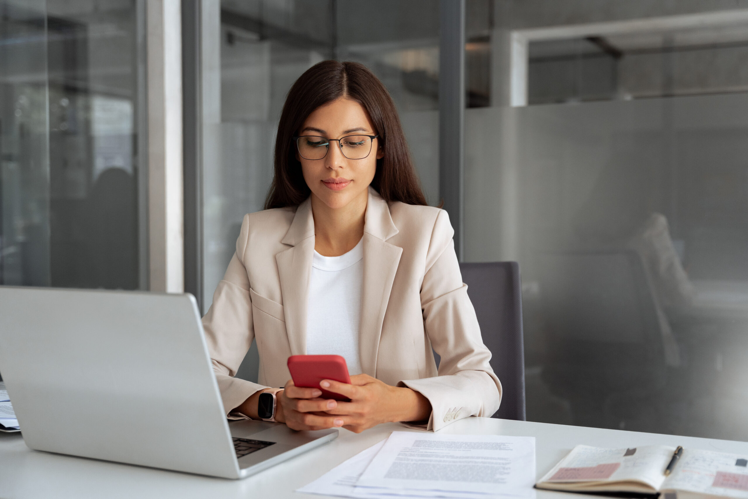 Hispanic business woman working on smartphone mobile phone at office workplace. Young specialist businesswoman manager using pc cell technology device finance bank app, chatting at work. Copy space